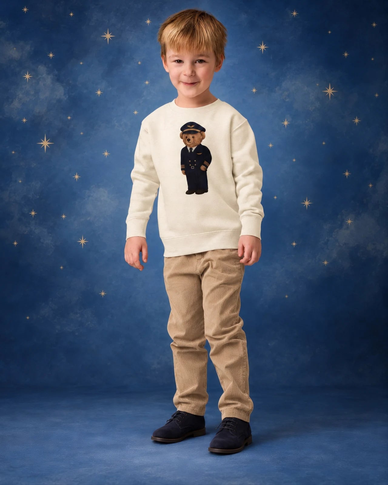 Bambino con la felpa color crema con orsetto pilota su uno sfondo blu stellato
